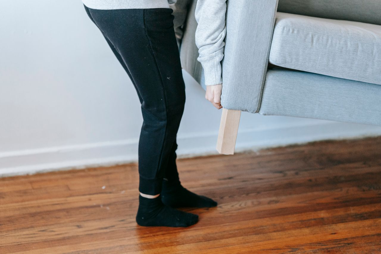 services-04 A person is lifting a couch in a minimalist living room with wooden floors.